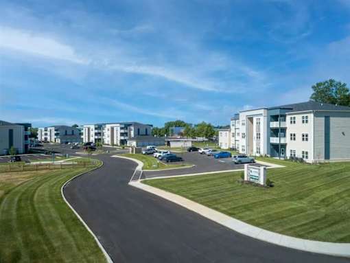 A road curves through a grassy area with apartment buildings in the background.