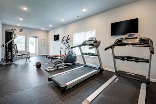 A spacious home gym with treadmills, elliptical machines, and a television.