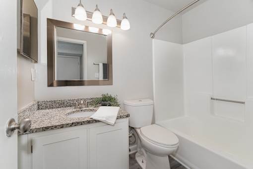A white bathroom with a granite countertop and a white toilet.