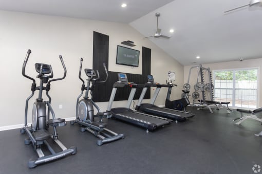 a gym with treadmills and weights and a tv on the wall