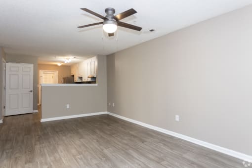 an empty living room with a ceiling fan and a kitchen
