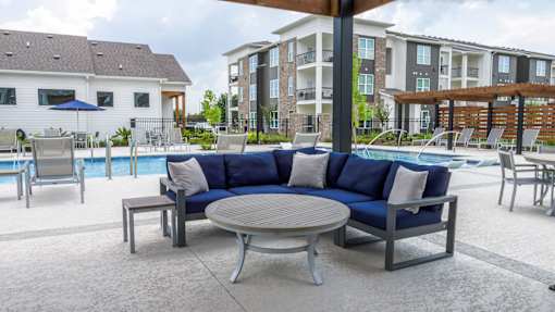 A blue sofa with white pillows is in the foreground of a poolside area.