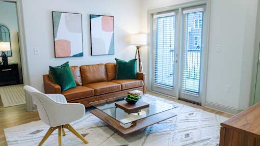 A living room with a brown leather couch, a white chair, and two abstract paintings on the wall.