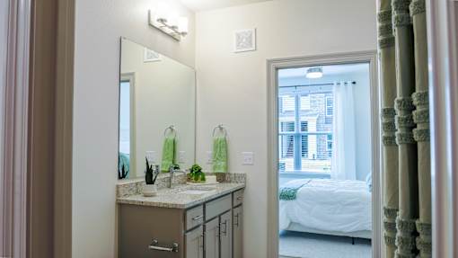 A bathroom with a sink, mirror, and a bedroom in the background.