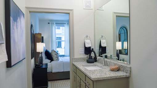 A bathroom with a sink, mirror, and a bedroom in the background.