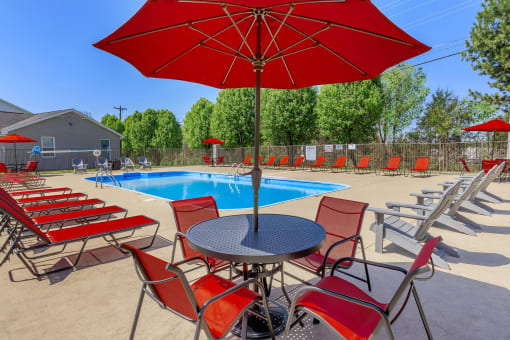 a pool with red chairs and a table with an umbrella at The Dylan, Murfreesboro, TN 37129