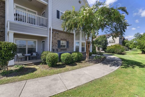 a sidewalk in front of a building with trees and bushes