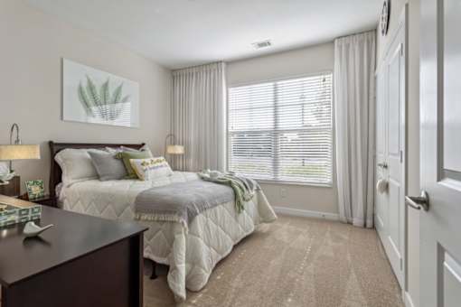 A bedroom with a large bed and a window with blinds.at Century Hampton Roads, Suffolk, VA  