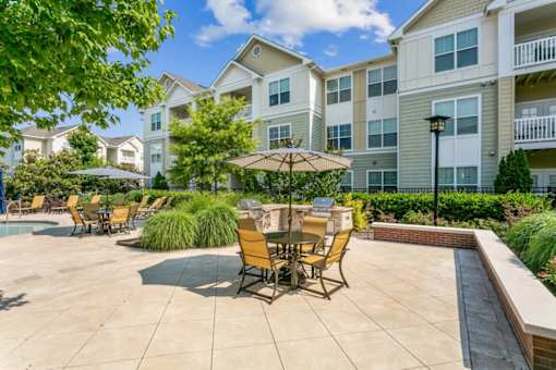 A patio with chairs and an umbrella in front of apartment buildings.at Century Hampton Roads, Virginia, 23435