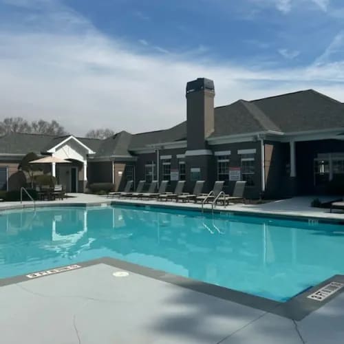 A swimming pool in front of a building with a row of chairs.