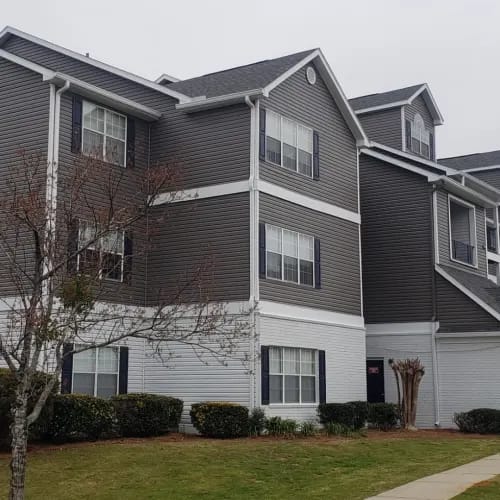 A grey and white apartment building with a tree in front.