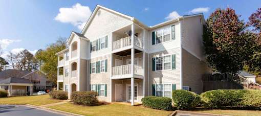 A large, modern apartment building with multiple balconies and green shutters on the windows.