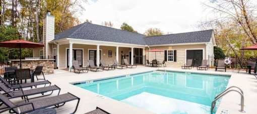 A pool in a backyard with a house and patio furniture.