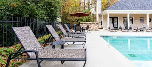 A poolside area with lounge chairs and a house in the background.