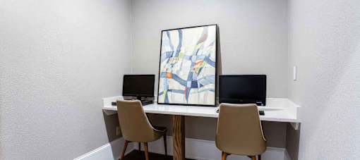 A white desk with two chairs and a painting on the wall.