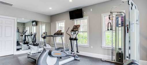A spacious home gym with a treadmill, elliptical machines, and a television.