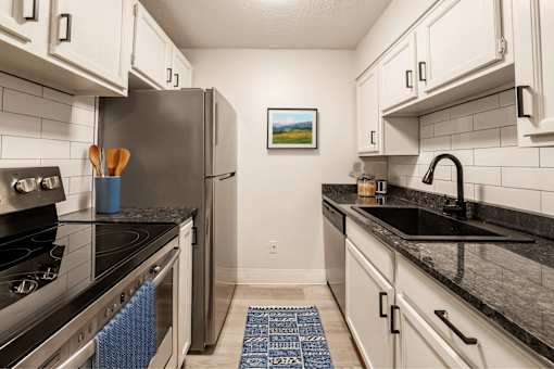 A kitchen with a black counter top and a fridge.
