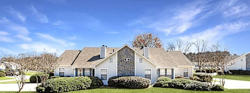 A large house with a grey roof and white walls is surrounded by a well-manicured lawn.