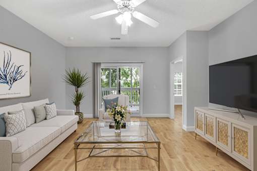 A living room with a white couch, a glass coffee table, and a painting on the wall.