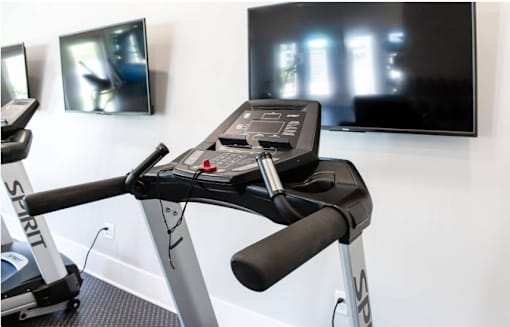 A treadmill with a black seat and handlebars is in a room with a TV mounted on the wall.