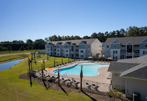 A swimming pool is surrounded by a fence and chairs in front of a building.