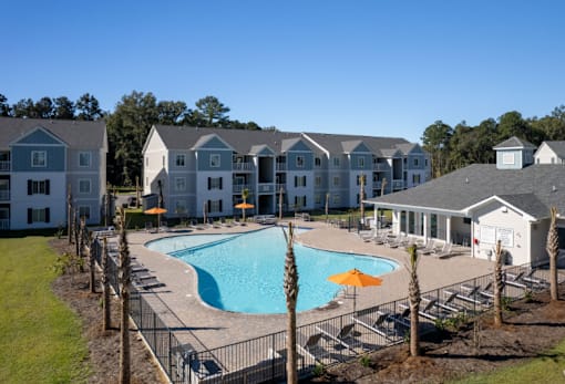 A large swimming pool surrounded by a fence and chairs with a building in the background.