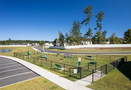 A park with a paved walkway, green benches, and a fence.