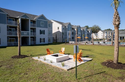 A modern outdoor seating area with orange chairs and a white table is set up in front of a row of apartment buildings.