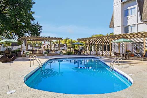 A large outdoor swimming pool with a wooden pergola and lounge chairs.