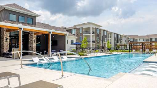 A large swimming pool with lounge chairs and a building in the background.