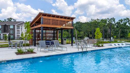 A pool area with a wooden pavilion and lounge chairs.