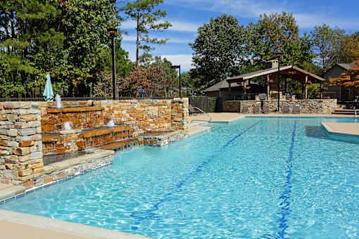A large swimming pool with a stone wall and a small gazebo in the background.