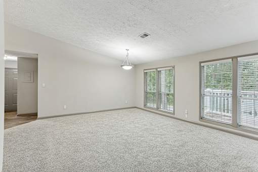 A spacious room with a carpeted floor and a window with blinds.