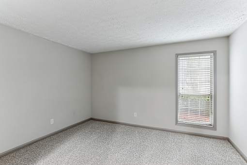 A room with a window and a carpeted floor.