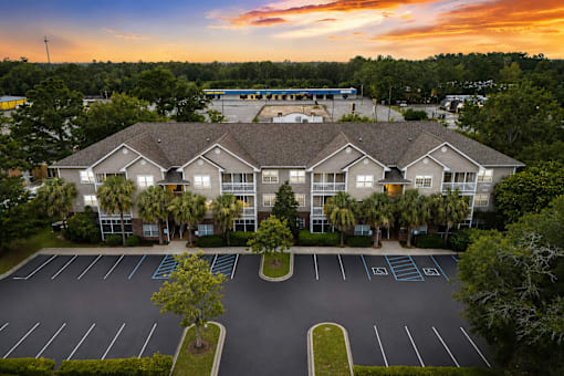 A parking lot in front of a building with trees and a sunset in the background.