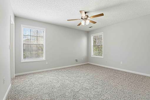 A room with a ceiling fan and two windows with blinds.