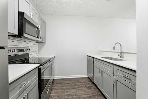 A kitchen with a black microwave above a stove and a white countertop.