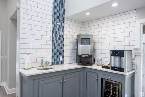 A kitchen with a white tiled wall and a grey cabinet.