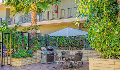 a patio with a grill and a table with chairs and an umbrella