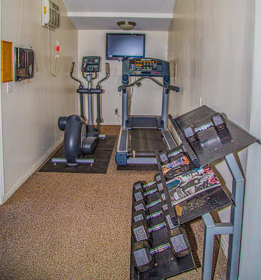 a room with a treadmill and a table with a television on the wall