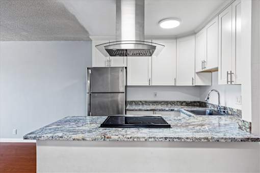 A kitchen with a marble countertop and a stainless steel refrigerator.