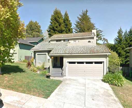 A house with a grey garage door is surrounded by greenery.