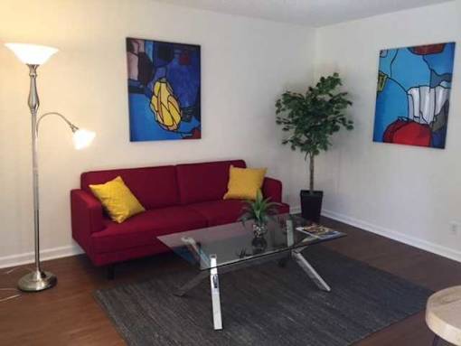 A red couch with yellow pillows sits in a living room with a glass coffee table.