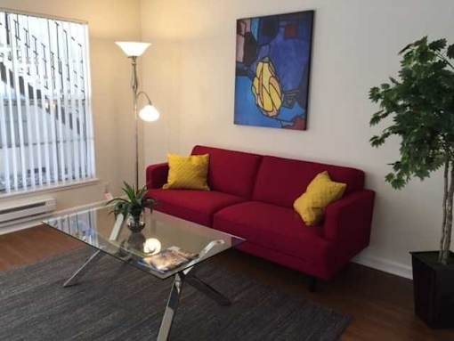 A red couch with a yellow pillow is in the middle of a room with a glass table in front of it.