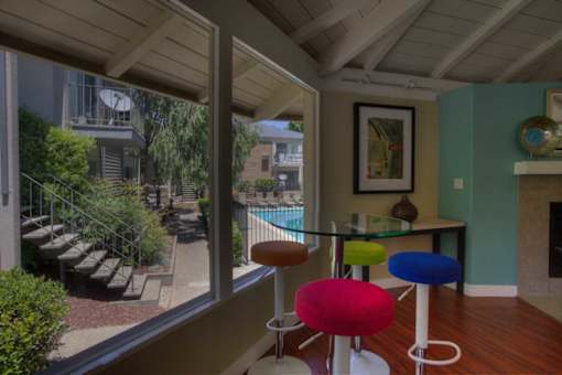 A room with a glass table and four colorful stools.