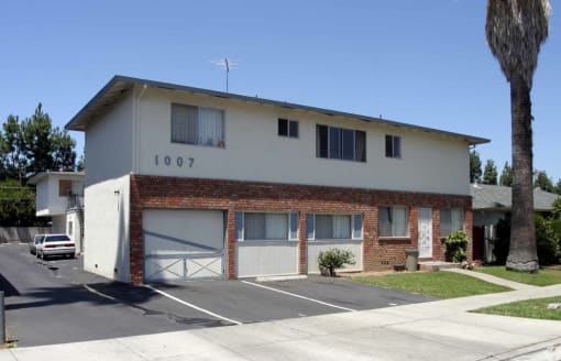 The front view of Prodesse Property Group 1007 Leigh AvenueSan Jose, CA 95128 the apartment community is white and brick wall with three garages and driveways a palm tree is in the right hand corner
