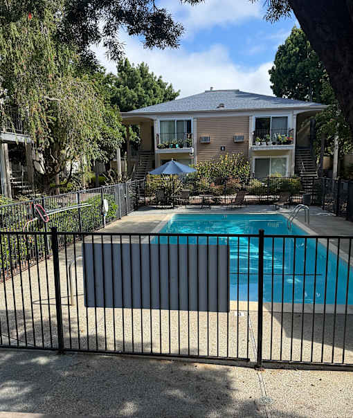 A black fence surrounds a small pool in front of a two-story house.