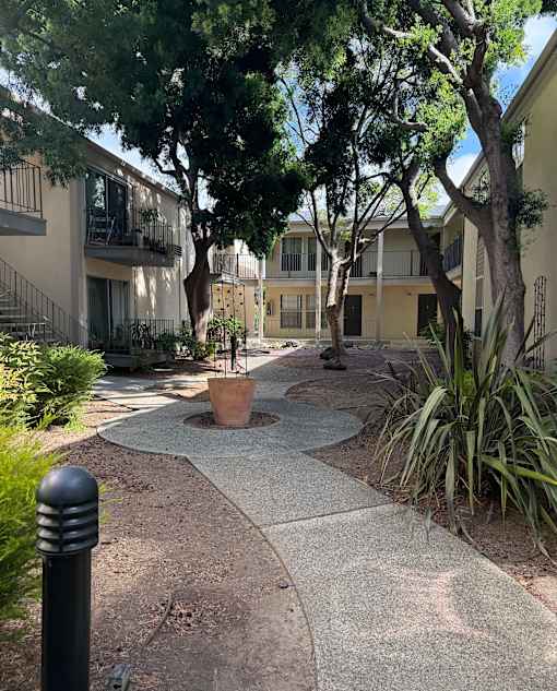 A concrete walkway leads through a landscaped courtyard between two apartment buildings.