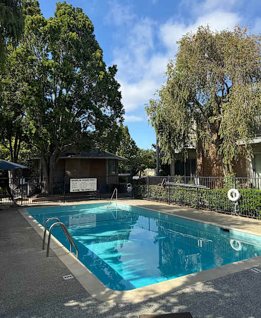 A pool surrounded by trees and a fence with a sign on it.