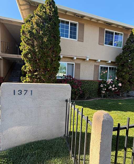 A white sign with the number 1371 on it is in front of a house.